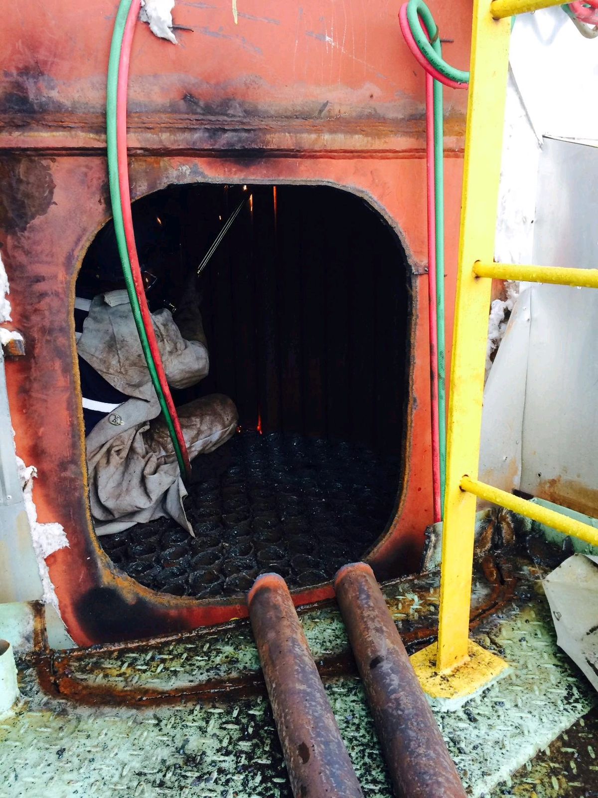 Trabalhador dentro de uma câmara de caldeira industrial enferrujada, pronto para iniciar a limpeza interna.