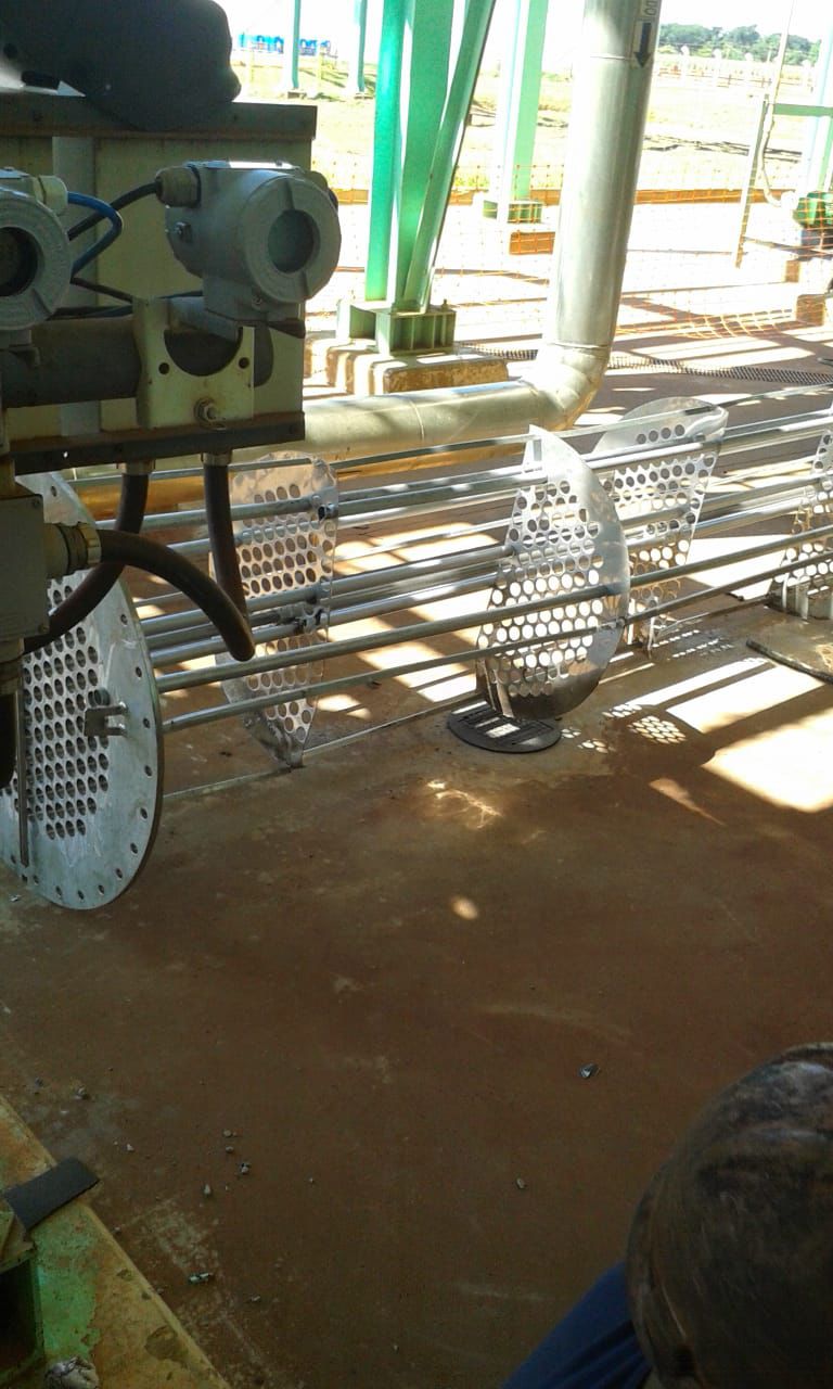 Componentes de um trocador de calor: placas perfuradas e tubos metálicos em uma área de serviço.